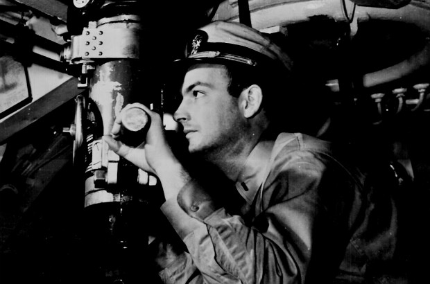 An officer looking through the periscope in the control room of a U.S. Navy submarine in World War II.